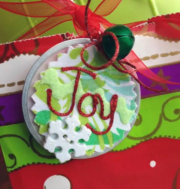 Kreinik Iron-on Metallic Threads "write" the word Joy on this recycled gift tag.
