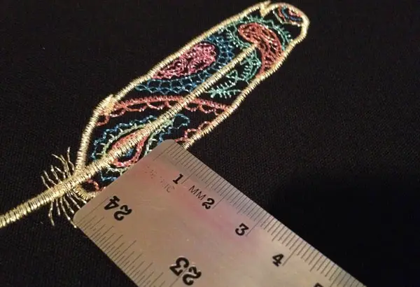 Measuring an embroidered feather made of metallic thread with a metric ruler.
